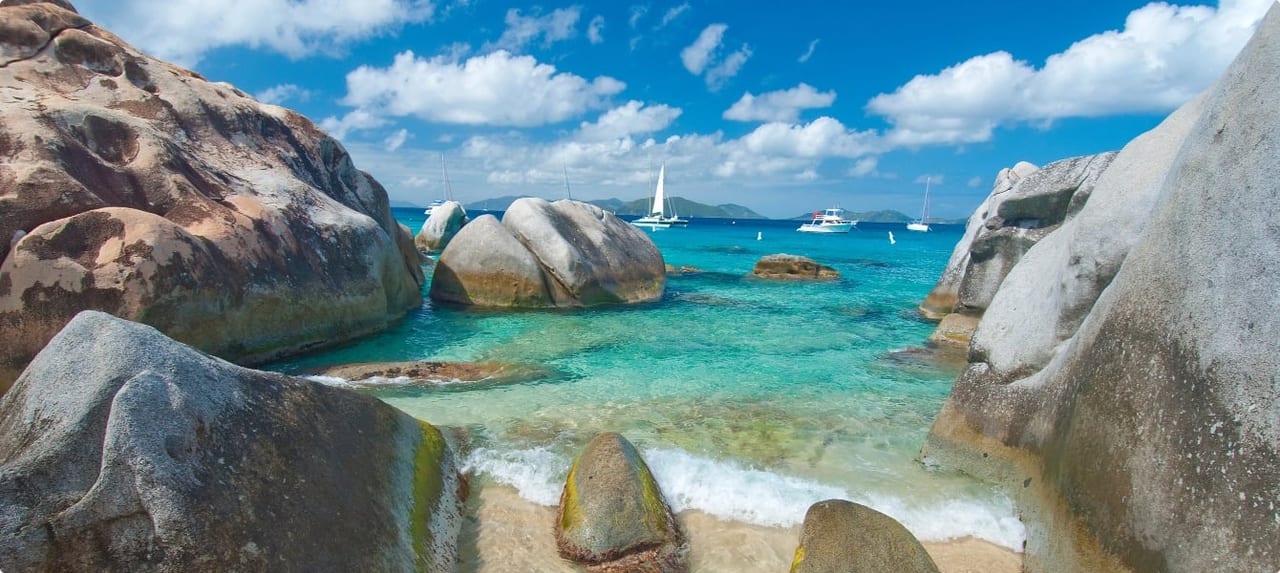 Aerial view of a secluded BVI island with white sand beach, tropical vegetation, and vivid blue-green water