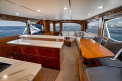2020 Viking 68 Convertible - Salon interior with dinette table, L-shaped sofa, galley counter and television