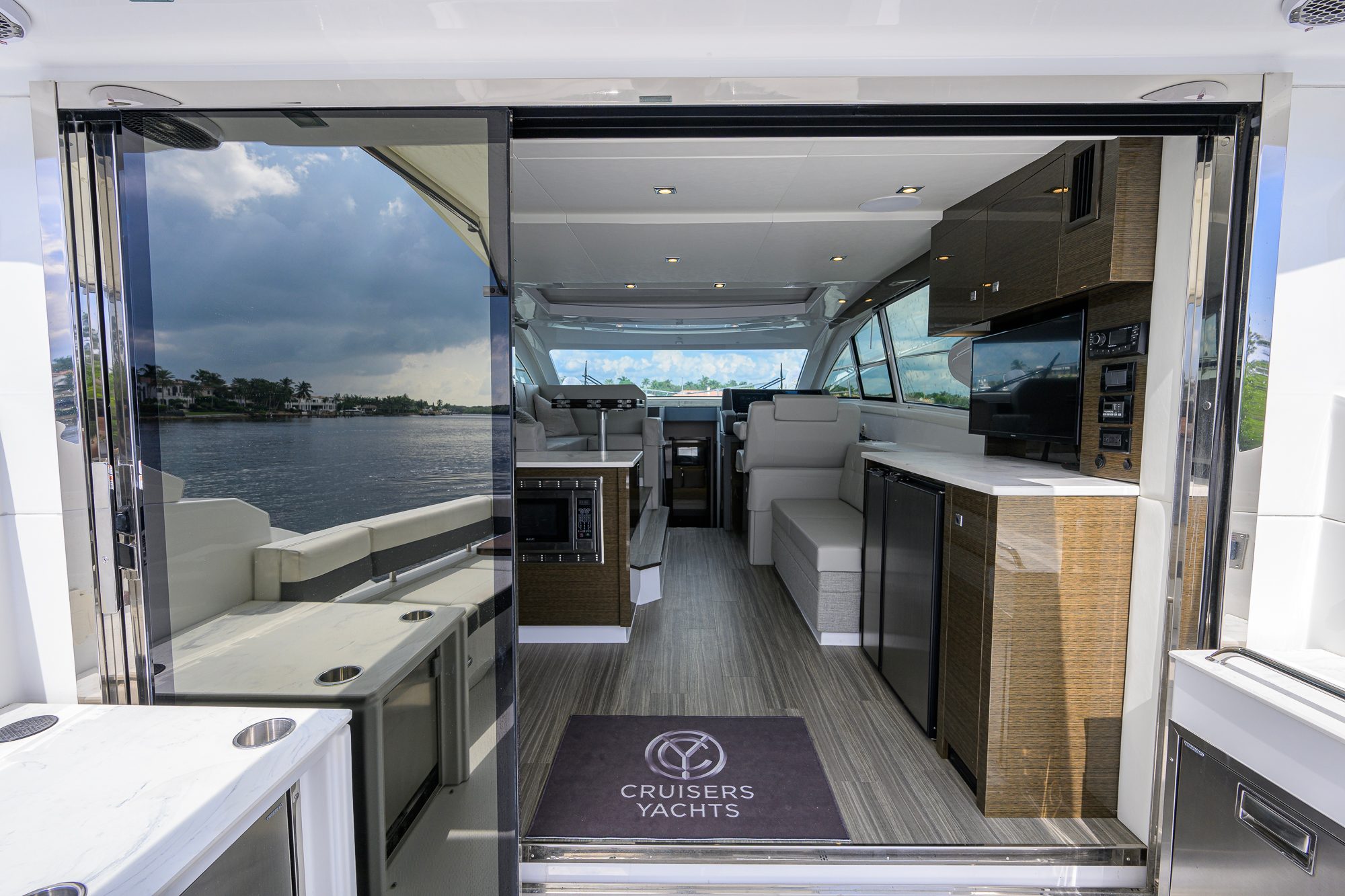 2020 46 Cruisers Cantius - View through open glass doors into salon with seating, galley and television