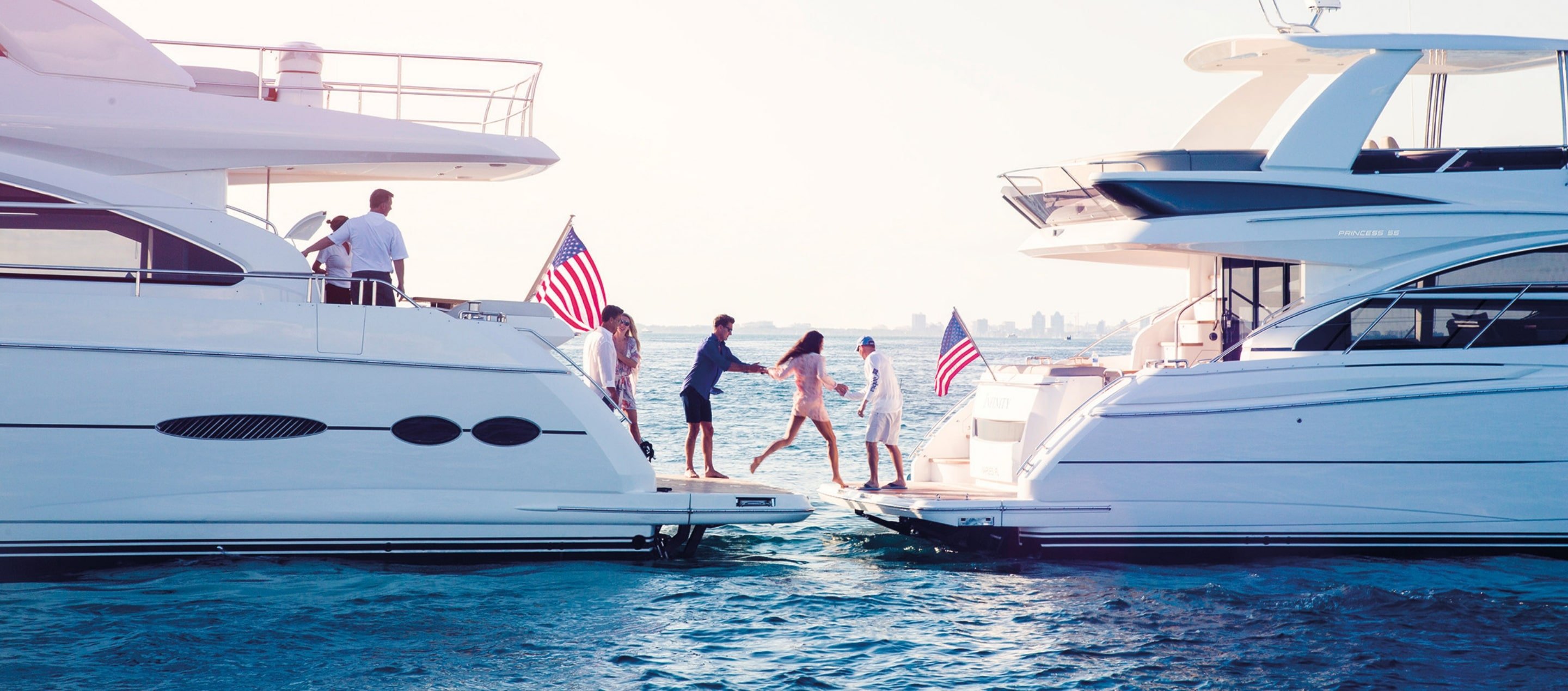 Two luxury yachts connected with people enjoying on the water under a sunny sky, featuring the HMY Yachts lifestyle Two luxury yachts connected with people enjoying on the water under a sunny sky, featuring the HMY Yachts lifestyle