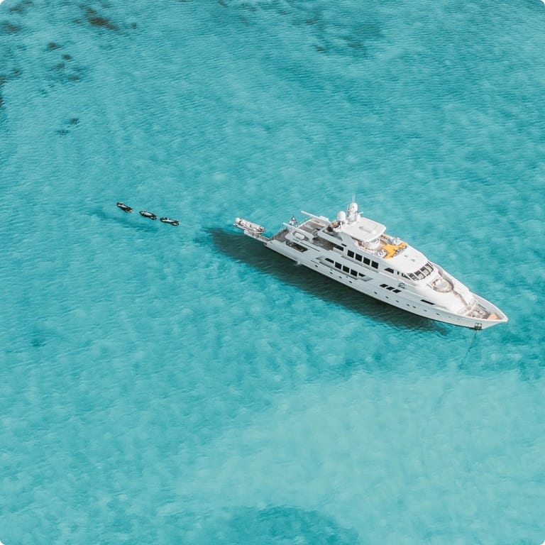 Swimming pigs wading in the crystal-clear tropical waters of the Bahamas with a yacht visible in the background