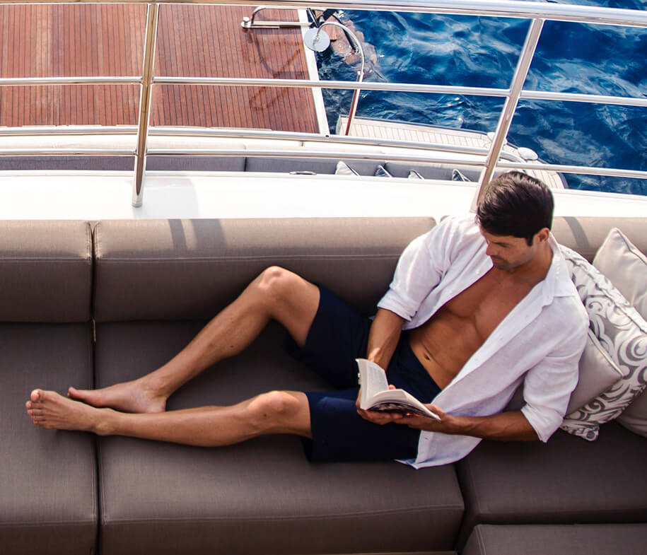 Man relaxing on sofa on the back of a yacht reading a book